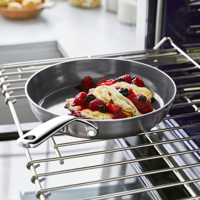 Stainless steel 8-inch frypan with mirror handle, holding pancakes and berries on an oven rack.