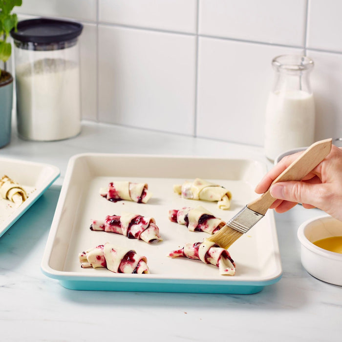 Hand brushing egg wash onto berry pastries on a 13 x 9 GreenLife ceramic nonstick cookie sheet set.