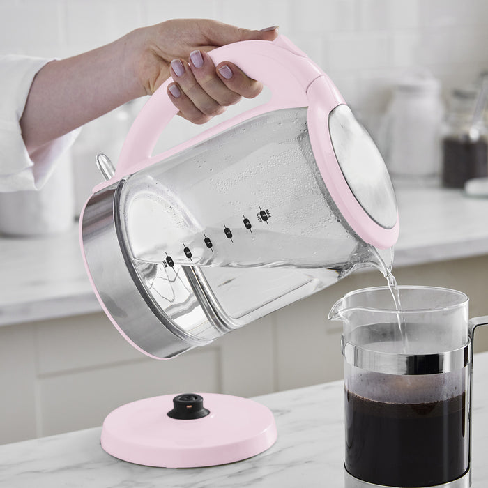 Pink GreenLife glass electric kettle pouring hot water into a French press on a kitchen counter.