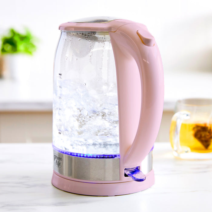Pink glass electric kettle on a kitchen counter next to a cup of tea and a small green plant.