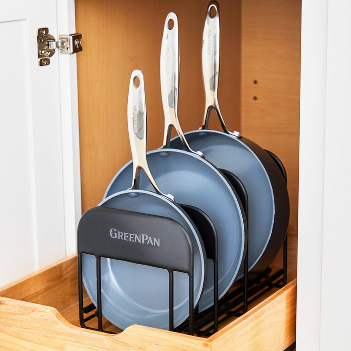 Three green frying pans in a metal rack, organized inside a kitchen drawer.