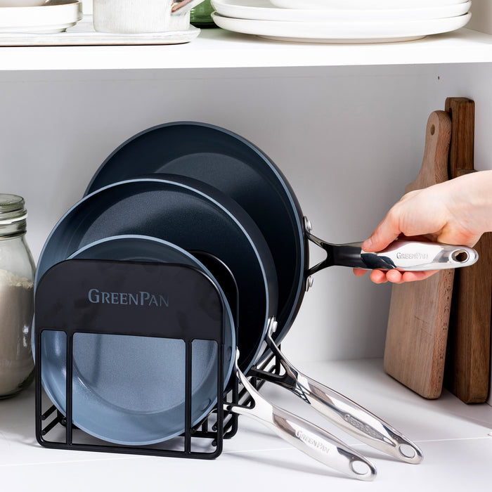 Hand reaching for a frying pan from a rack holding several nested pans on a kitchen countertop.