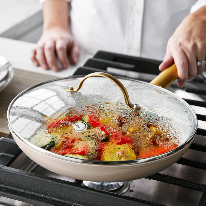 GreenPan Reserve 10 skillet with matte gold handle on stove, glass lid covering sautéed vegetables.