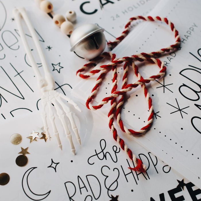 Silver bell with a red and white string and a plastic skeleton hand on top of advent paper