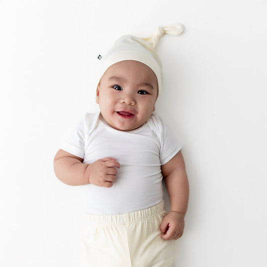 Smiling infant wearing the Knotted Cap in Chamomile with matching pants and white short sleeve bodysuit