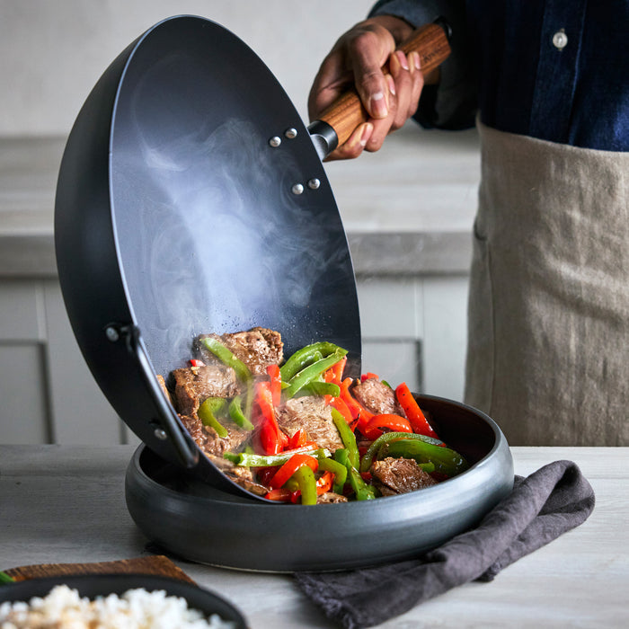 Person cooking in a wok with vegetables and meat on a kitchen counter.