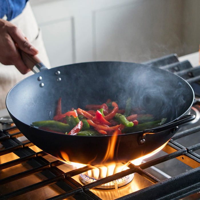 Wok with vegetables being cooked over a flame on a stove