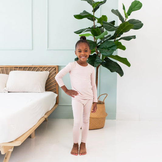 Smiling toddler standing in front of a fig tree while wearing Long Sleeve Pajama Set in Blush
