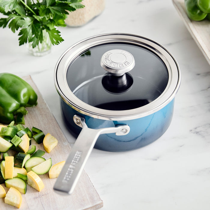 Aegean teal 1.5-quart saucepan with lid on marble, surrounded by chopped green and yellow vegetables.