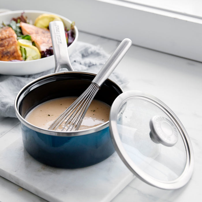 Aegean teal 1.5-quart enameled steel saucepan with sauce and whisk on a marble countertop.