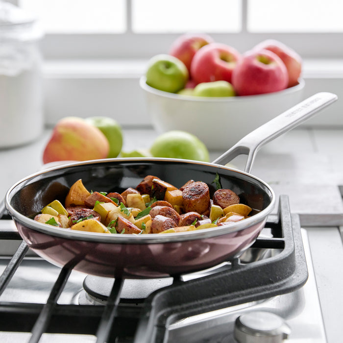 Sausage and apple slices cooking in a Merten  Storck 9.5-inch frypan, apples in a bowl and on counter behind.