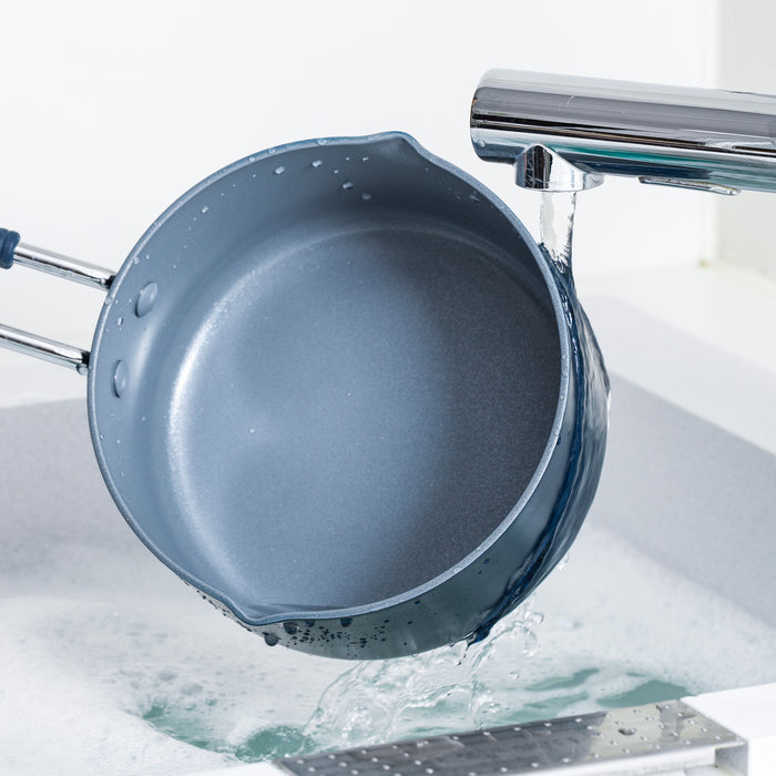Navy ceramic 1-quart saucepan being rinsed with soapy water under a kitchen faucet.