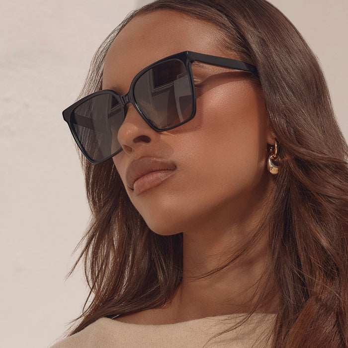 lifestyle - female business woman wearing iconica diff eyewear naomi square oversized sunglasses with a black acetate frame and grey gradient polarized lenses angled view