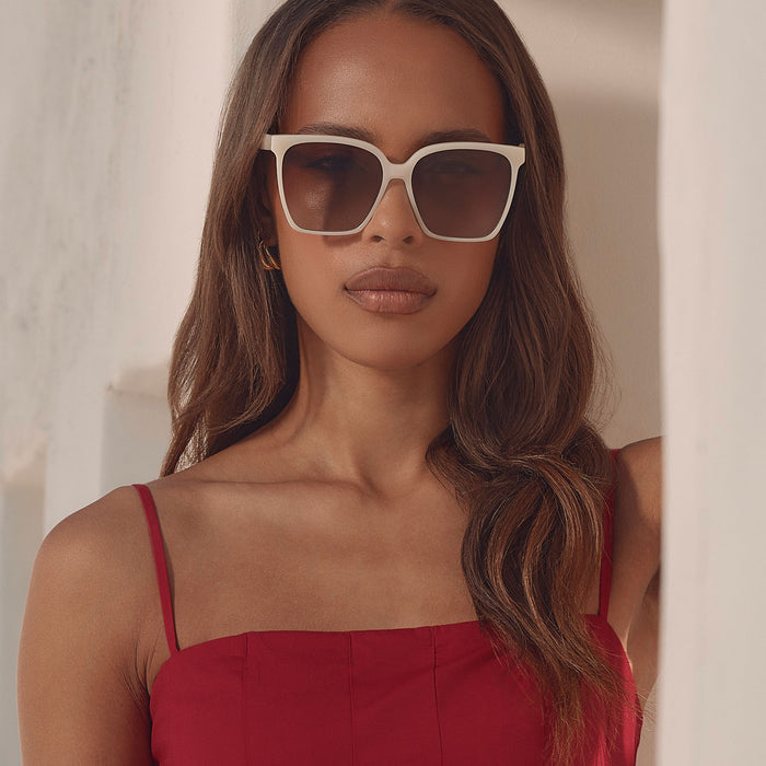 lifestyle - female at a resort wearing iconica diff eyewear naomi square oversized sunglasses with a meringue cream colored acetate frame and brown gradient polarized lenses front view
