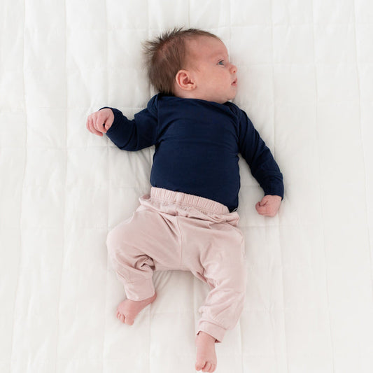 Newborn wearing Kyte Baby Pants in Blush and Long Sleeve Bodysuit in Navy