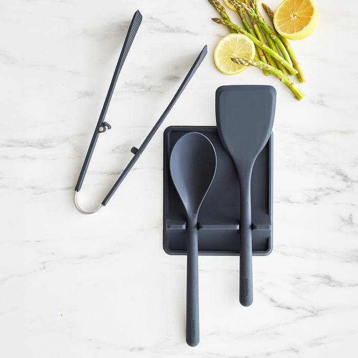 Gray silicone 4-piece utensil and tool rest set on marble with metal tongs, lemon slices, and asparagus.