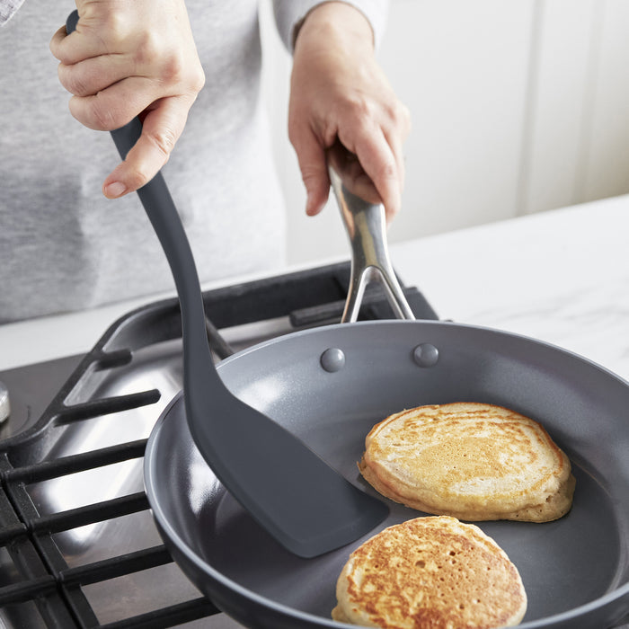 Gray silicone 4-piece utensil and tool rest set beside a frying pan as someone flips pancakes.