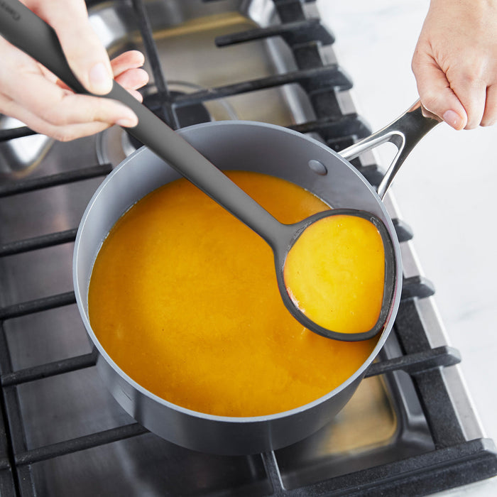 Person using a silicone ladle to remove broth from a saucepan