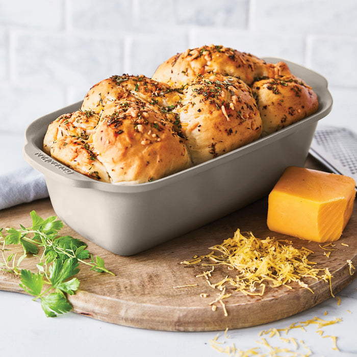 Golden herb-topped bread in a white ceramic nonstick pan, with parsley and cheddar placed beside it.