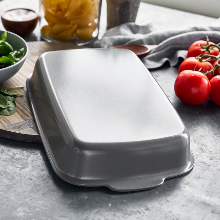 Ceramic nonstick 13x9 baker on a counter with fresh tomatoes, spinach, and uncooked pasta nearby.