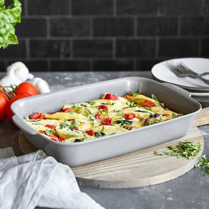 Gray ceramic nonstick 13x9 rectangular baker with stuffed pasta shells, resting on a wooden board.