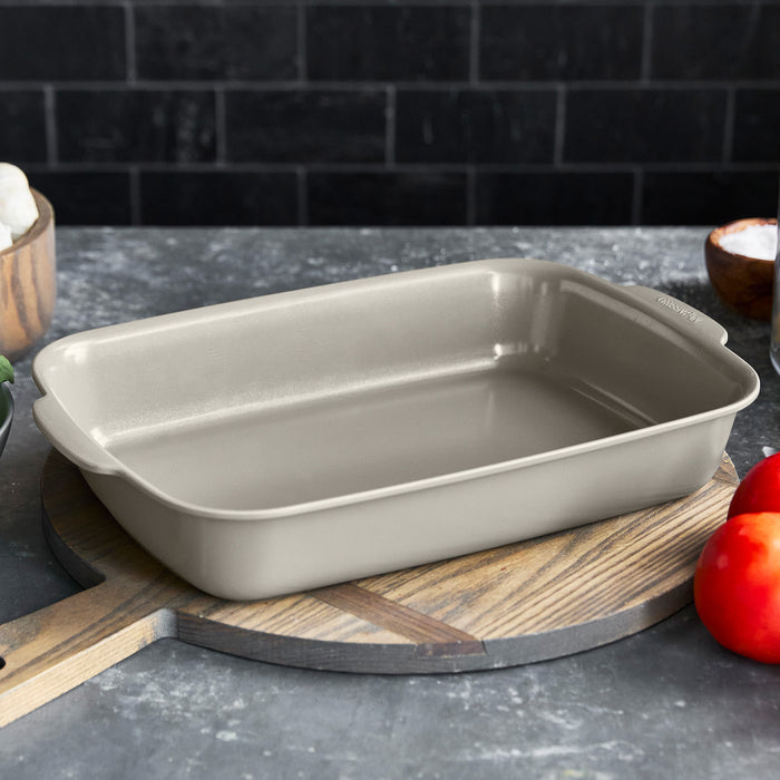 Taupe ceramic nonstick rectangular baker on a wooden board with red tomatoes beside it.