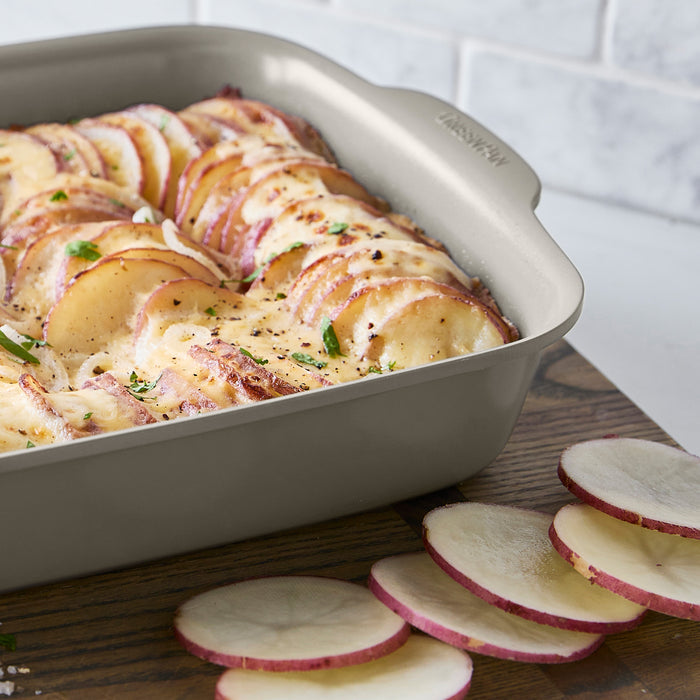 Cheesy baked potatoes with herbs in a white ceramic 13x9 rectangular baker.