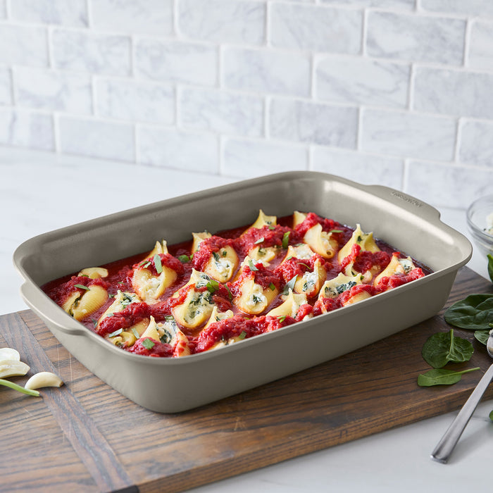 Two taupe ceramic nonstick cake pans with pasta shells, displayed on a wooden board. Set includes two pieces.