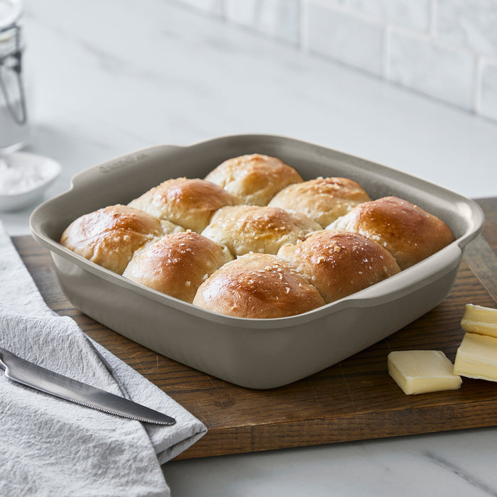 Two taupe ceramic nonstick cake pans on a wood board with a slab of butter and a knife nearby. Set includes 2 pans.