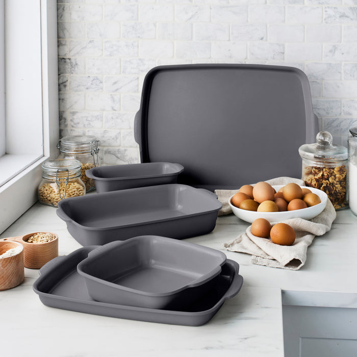 Gray ceramic nonstick 5-piece cookware set on a kitchen counter with eggs, grains, and spices nearby.