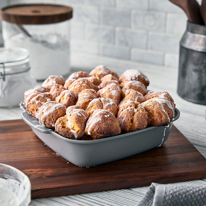 Gray ceramic nonstick bakeware set holding iced pull-apart bread, displayed on a wooden board. Set includes 5 pieces.
