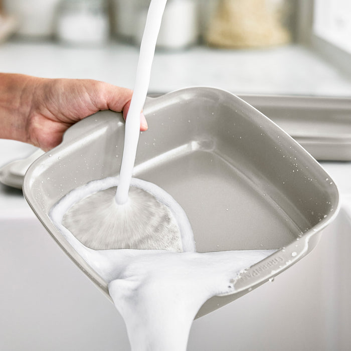 Ceramic nonstick 8x8 square baker with built-in handles being washed in a bright kitchen sink.