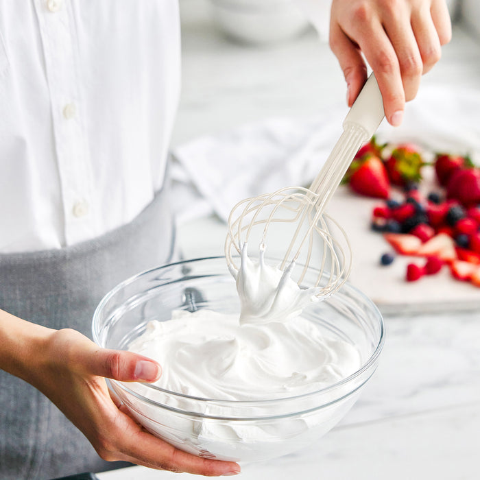 Bisque silicone 8-piece utensil set with crock on countertop, whipping cream; fresh fruit nearby.
