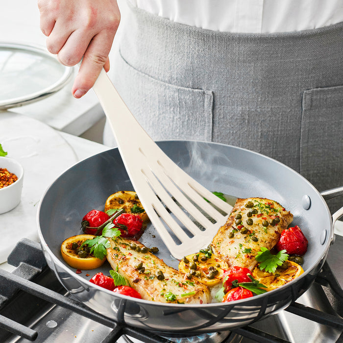 Premiere Silicone 8-piece utensil and crock set in bisque on kitchen counter, with fish fillets and lemons being cooked.