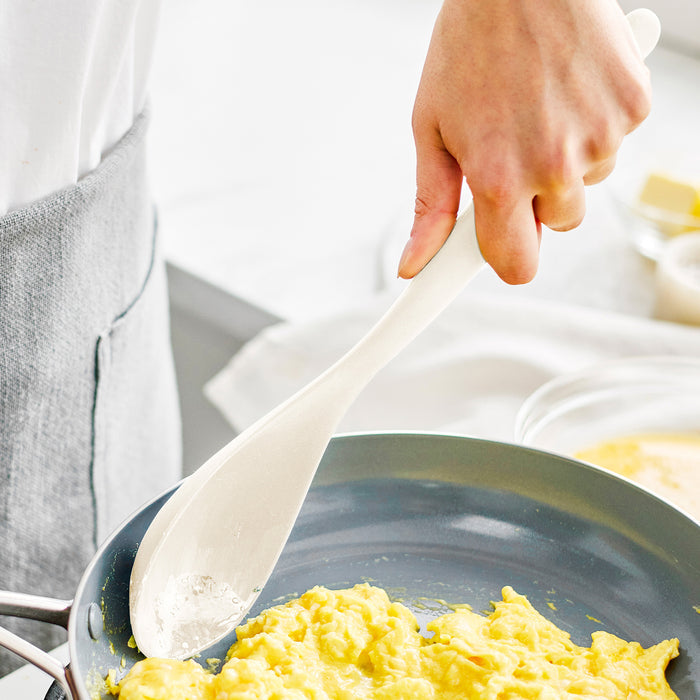 Person stirring scrambled eggs with a beige silicone utensil from an 8-piece set in a bright kitchen.