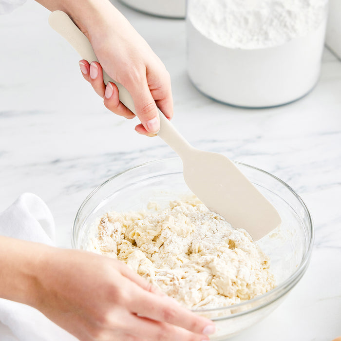 Silicone 8-piece utensil and crock set in bisque on a white countertop, some flour scattered nearby.