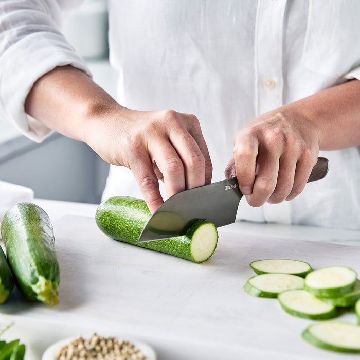 Slicing a zucchini on a white cutting board with a stainless steel Santoku knife from the Premiere Titanium Cutlery set.