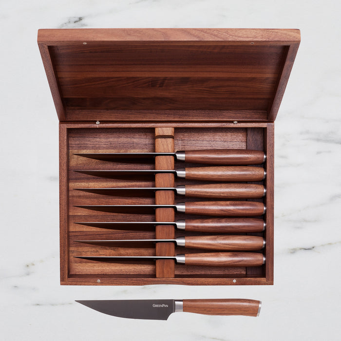 Eight steak knives with walnut handles displayed on a white marble surface.