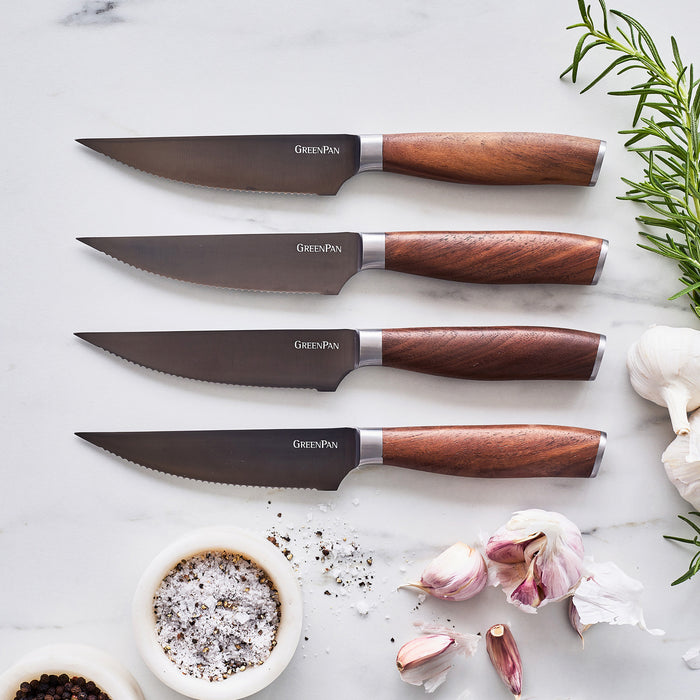 Eight-piece steak knife set with walnut handles arranged on a marble surface, surrounded by herbs and spices.