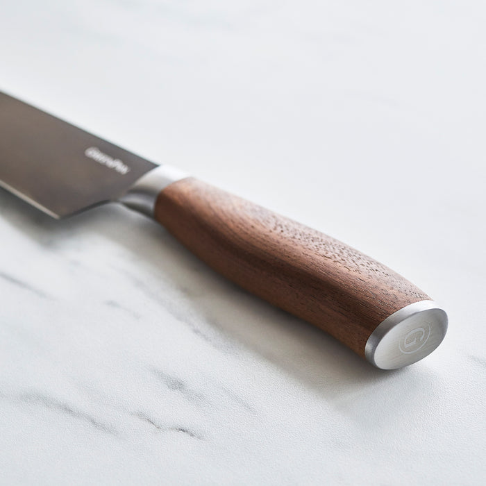 Set of steak knives with walnut handles on a white marble surface.