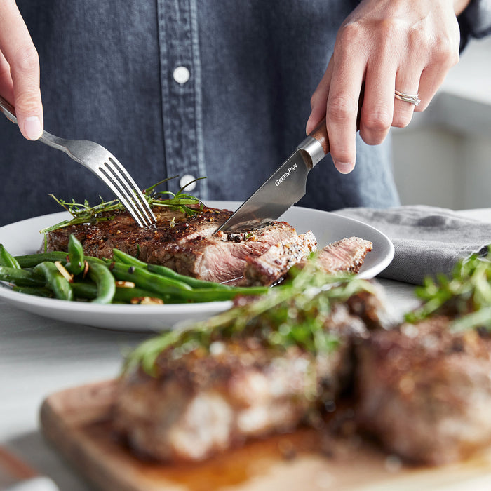A steak knife from the 8-piece Premiere Titanium Cutlery set slices steak and green beans on a white plate.