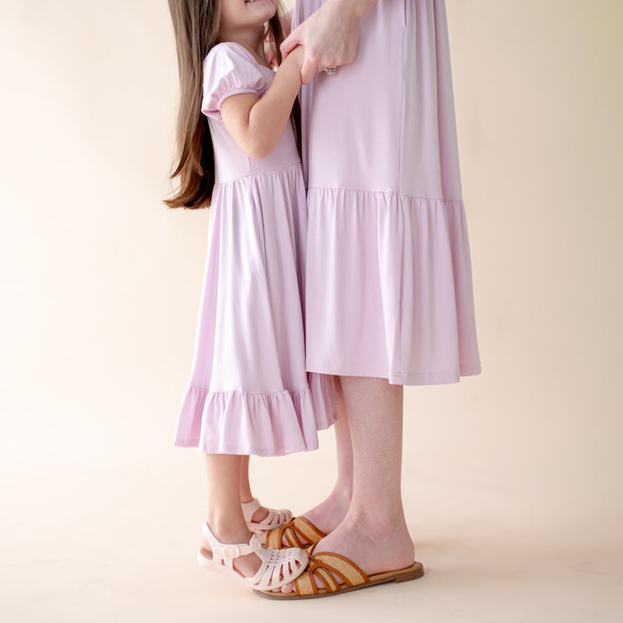 Two people wearing matching light purple dresses on a plain background
