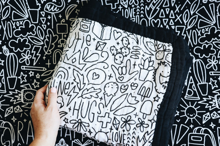 A hand holding the quilt folded in a square on a doodled background