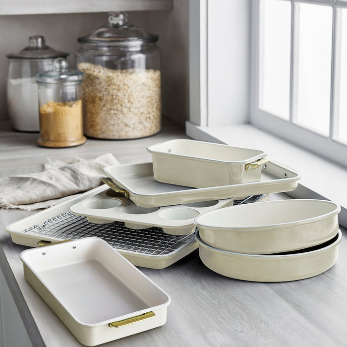 Cream-colored 8-piece bakeware set stacked on a kitchen counter beside jars of dry ingredients near a window.
