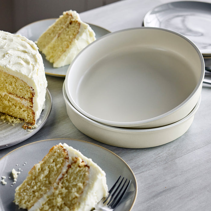 Eight-piece cream bakeware set on a table with two cake slices on plates and stacked bowls nearby.