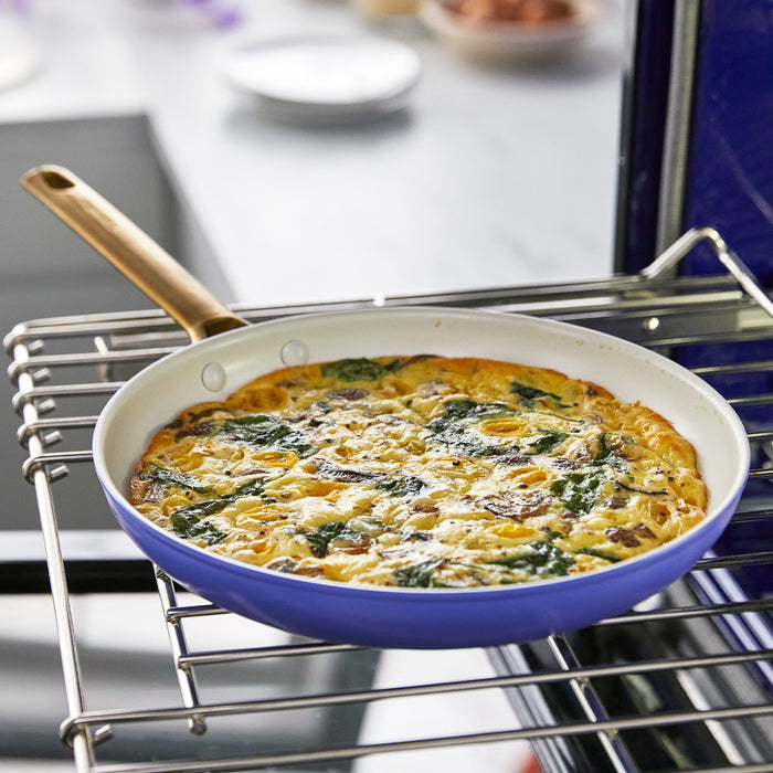 Spinach and cheese frittata cooking in a ceramic nonstick frypan set, wisteria color, golden top visible.