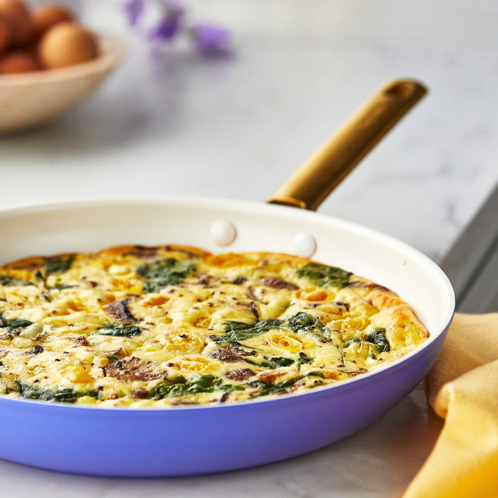 Vegetable frittata in a black ceramic nonstick frypan; eggs in a bowl are visible in the background.