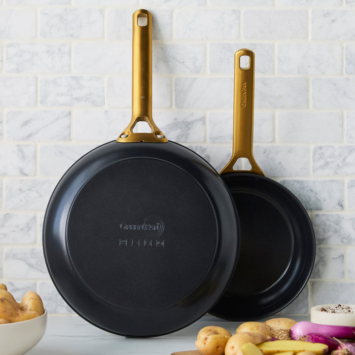 Two black frying pans with gold handles on a kitchen counter.