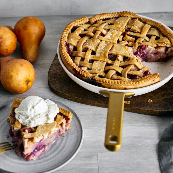 Pie with lattice crust on a wooden board, slice on a plate with whipped cream, and pears on the side.