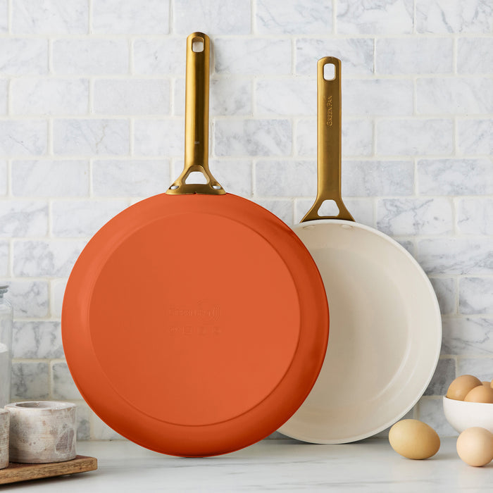 Two dark orange frying pans on a kitchen counter with a tiled wall background.